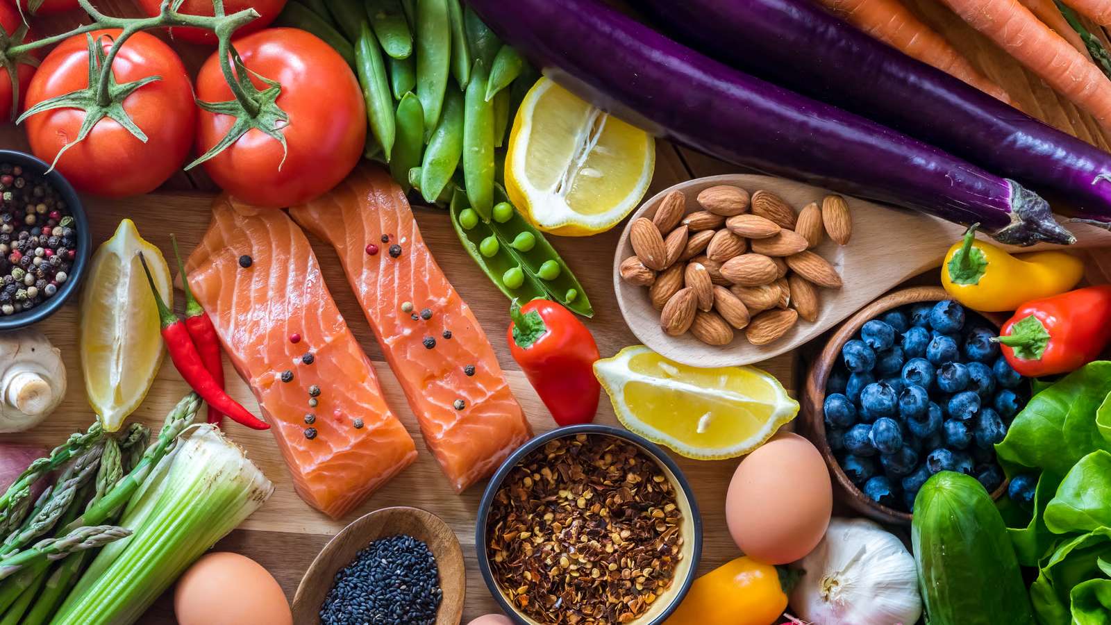 Aliments variés sur une table en bois — légumes, saumon, oléagineux, œufs